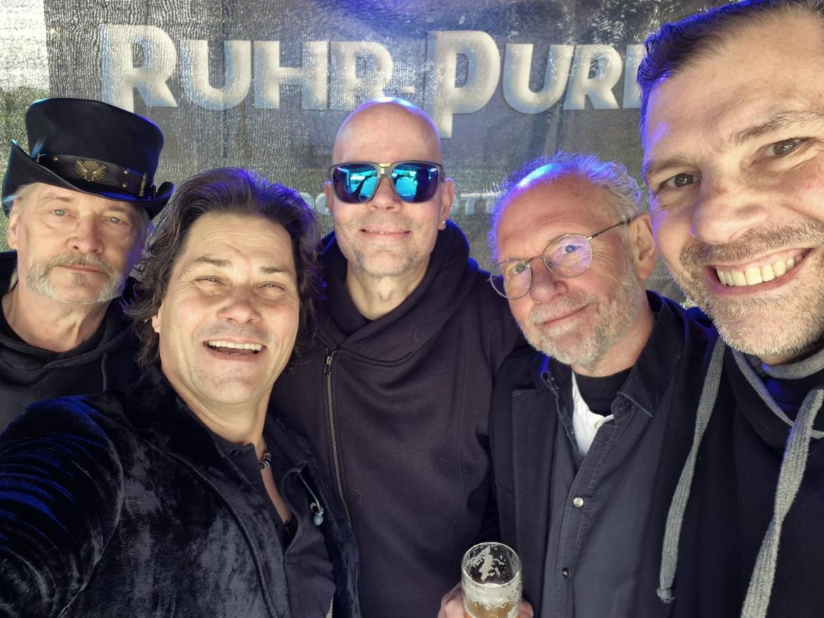 Fünf Männer machen ein Gruppen-Selfie vor einem Bühnenhintergrund mit der Aufschrift Ruhrpur.